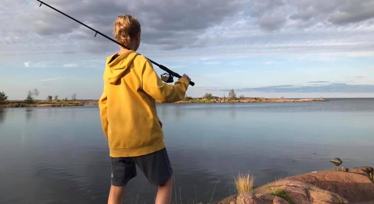 Pojke står och blickar ut över vattnet med ett fiskespö på axeln. 