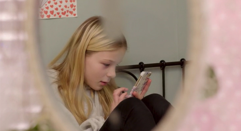Flicka sitter och läser på sin mobilskärm. 